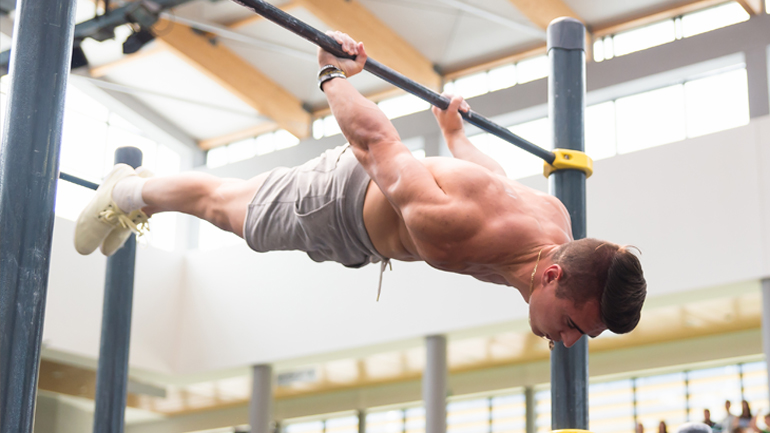 Mężczyzna ćwiczy na drążku, wykonując trudną figurę gimnastyczną w podporze tyłem.
